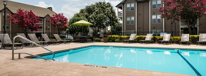 Inviting apartment community pool with sun loungers, vibrant landscaping, and modern buildings in the background.