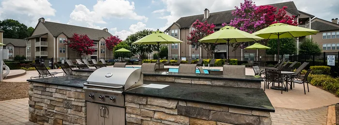 Charming community pool area with vibrant green umbrellas, modern grill, and lush gardens surrounded by beautiful apartment buildings.