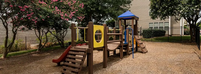 Inviting playground nestled under lush flowering trees, featuring a colorful slide and climbing structures in a serene neighborhood setting.