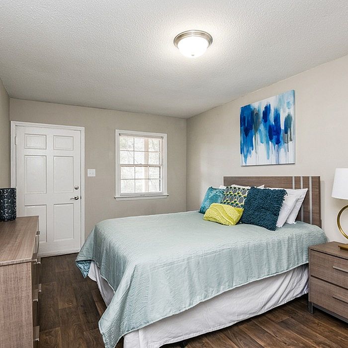Charming bedroom with modern decor, featuring a cozy bed adorned with colorful pillows, elegant wooden furniture, and vibrant abstract artwork.
