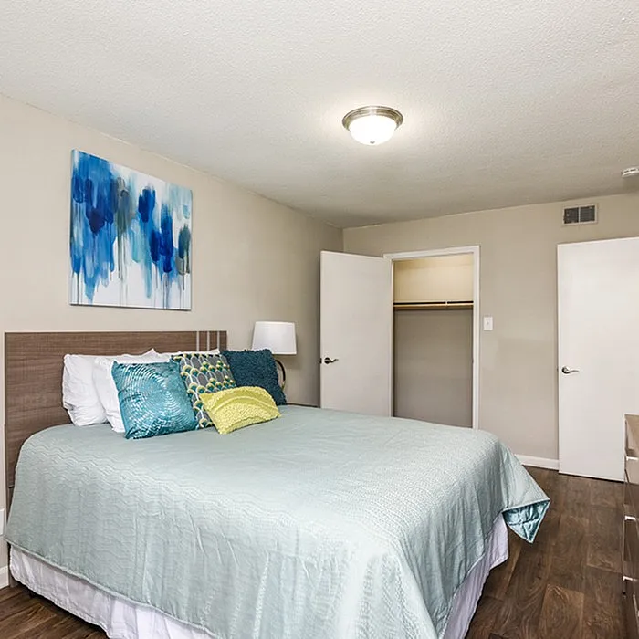 Inviting bedroom with elegant decor, featuring a soft blue bedspread, vibrant cushions, modern artwork, and sleek wooden flooring.