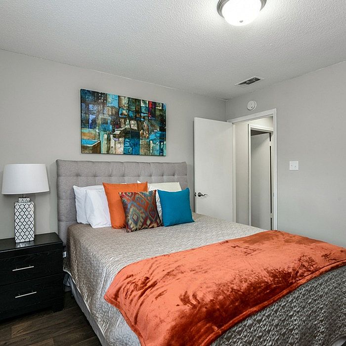 Cozy modern bedroom with plush gray headboard, vibrant orange and teal accent pillows, and modern artwork creating a stylish ambiance.