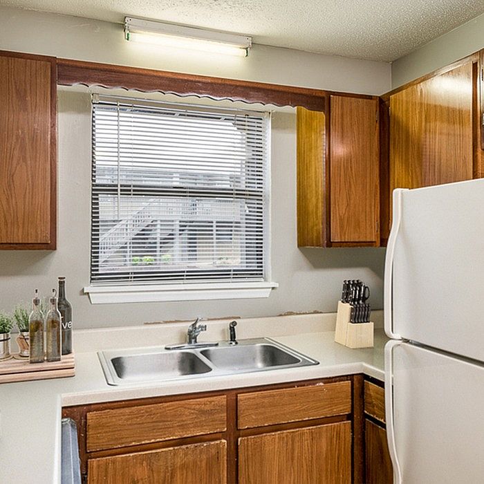 Inviting kitchen with warm wooden cabinets, dual sinks, and a view through stylish blinds, offering a cozy cooking space.