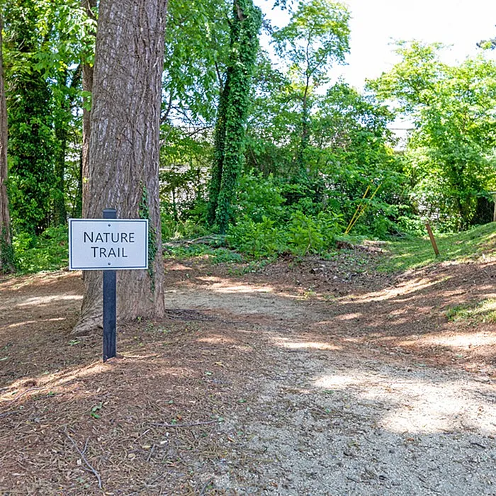 Inviting nature trail with lush greenery and a welcoming sign, perfect for outdoor enthusiasts.