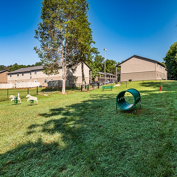 Charming apartment exterior view showcasing lush green outdoor space with play area, inviting benches, and scenic surroundings for relaxation.