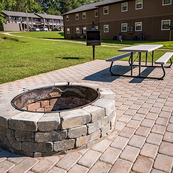Inviting outdoor patio with a cozy fire pit, modern grill, and spacious picnic table surrounded by lush greenery.