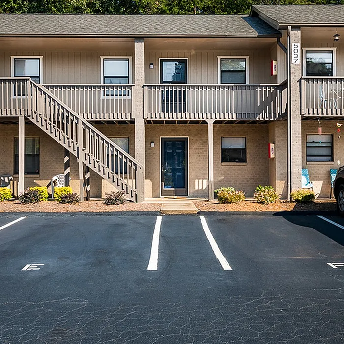 Charming two-story apartment building featuring a welcoming entrance and ample parking space, surrounded by manicured landscaping.
