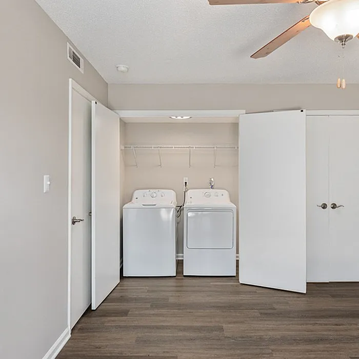 Modern apartment laundry nook featuring sleek washer and dryer, complemented by elegant wood flooring and efficient closet space.