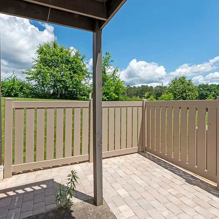 Charming outdoor patio with modern fencing, surrounded by lush greenery and a serene blue sky.