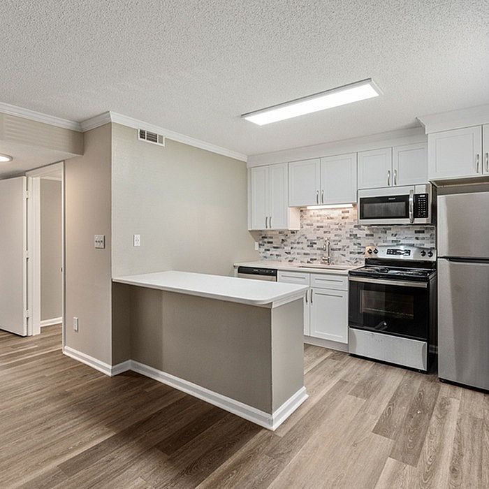Modern open kitchen with sleek stainless steel appliances, stylish backsplash, and elegant cabinetry, complemented by warm wood flooring.