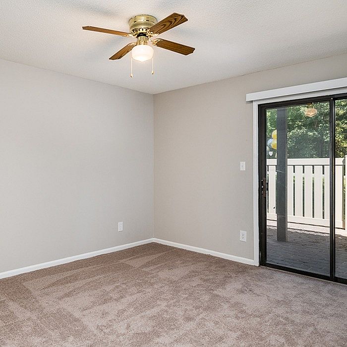 Bright, airy bedroom with plush carpet, ceiling fan, and large glass doors opening to a serene patio.