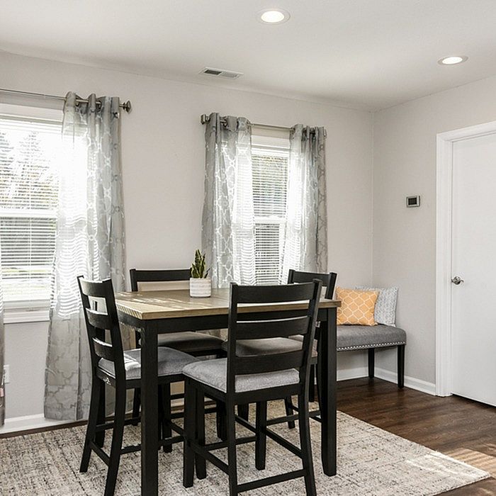 Bright and inviting dining area with a modern wooden table and black chairs, enhanced by natural light streaming through large windows with elegant curtains.