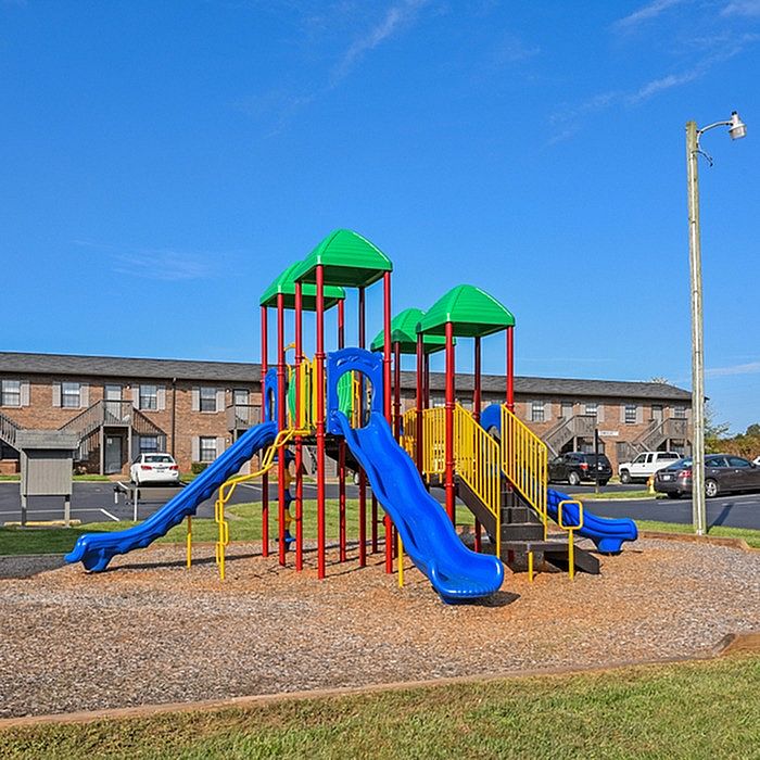 Bright and inviting playground with colorful slides and climbing structures, set in a vibrant community backdrop under a clear blue sky.