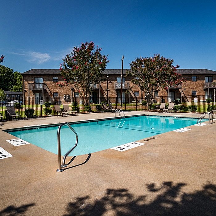 Inviting apartment complex with a refreshing outdoor pool surrounded by lush greenery and elegant lounge chairs.