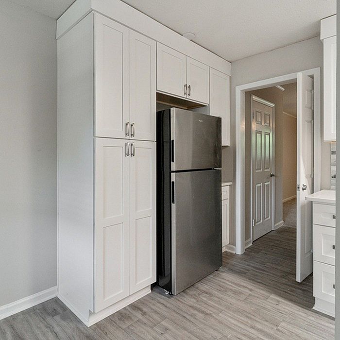 Modern kitchen design with sleek stainless steel refrigerator, elegant white cabinetry, and stylish wood flooring, offering a perfect blend of functionality and aesthetics.