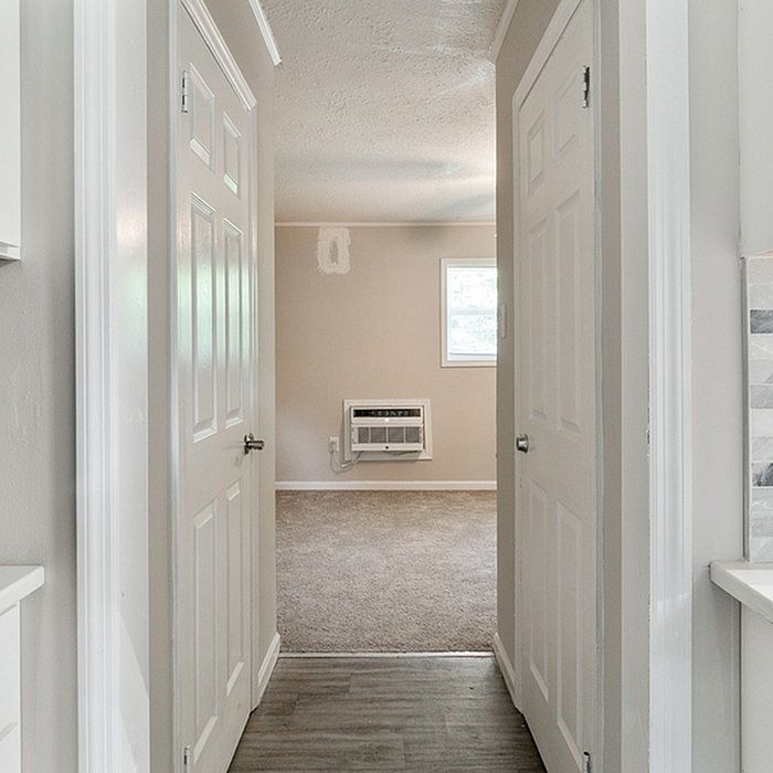 Inviting hallway leading to a bright, cozy room with plush carpeting and modern air conditioning unit.