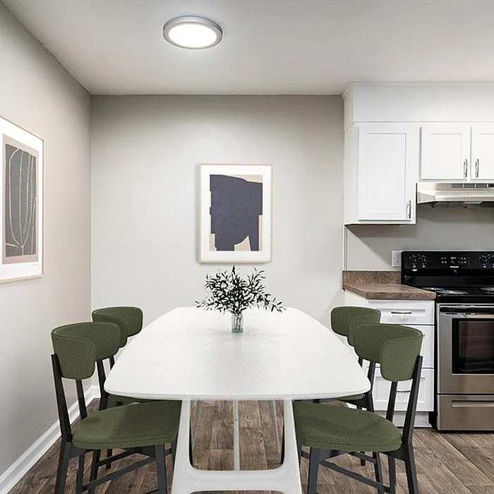 Modern kitchen and dining area featuring sleek white cabinetry, a stainless steel oven, and a stylish table with green chairs under warm lighting.