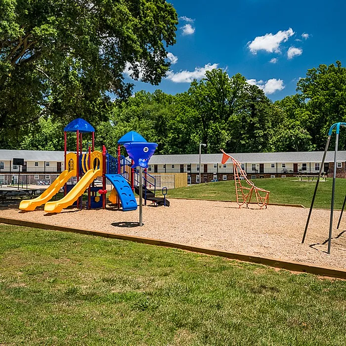 Inviting apartment community with vibrant playground set against lush green surroundings, perfect for families and outdoor fun.