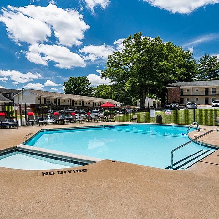 Inviting outdoor pool area with bright red lounge chairs and scenic green surroundings under a vibrant blue sky, offering a perfect relaxation spot.