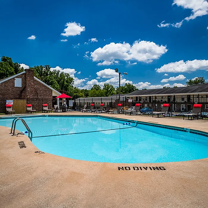 Inviting outdoor pool area with vibrant red lounge chairs under a clear blue sky, perfect for relaxation and enjoying sunny days.