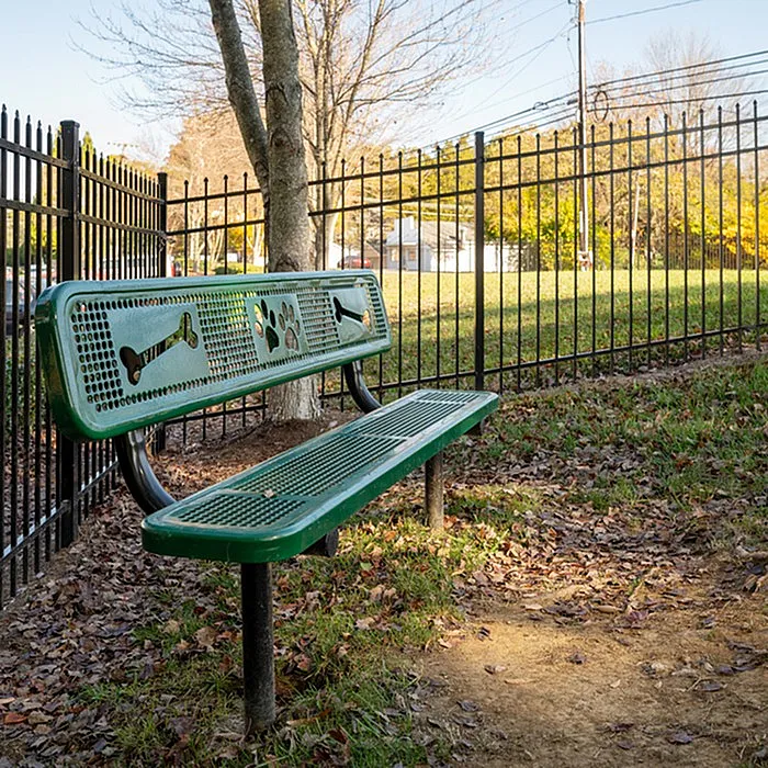Charming outdoor space featuring a green bench with playful bone and paw designs, surrounded by lush greenery and a secure fence, perfect for pet-friendly relaxation.
