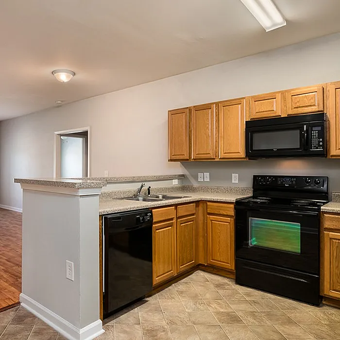 Modern kitchen with sleek black appliances, warm wooden cabinetry, and a cozy open layout leading into the living space.