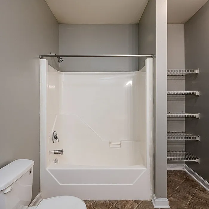 Modern apartment bathroom featuring a sleek white bathtub, elegant gray walls, and convenient built-in shelving, perfect for contemporary living.