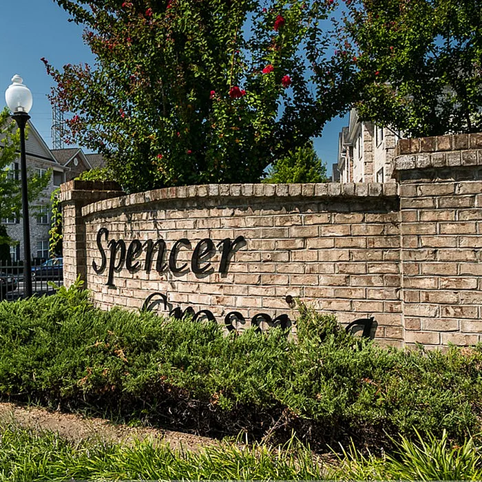 Inviting entrance to Spencer Crossing with lush greenery and brick sign, showcasing a charming community setting.
