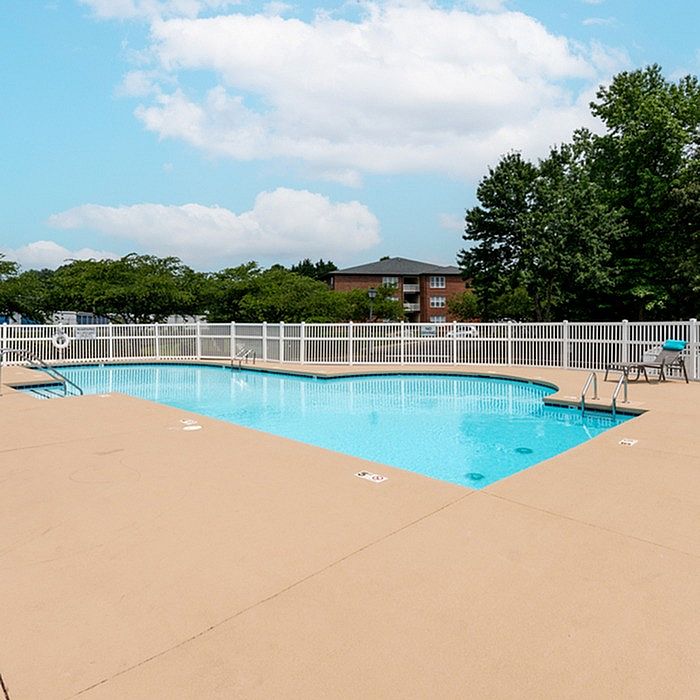 Inviting apartment complex pool with crystal-clear water, surrounded by a spacious deck and lush greenery.