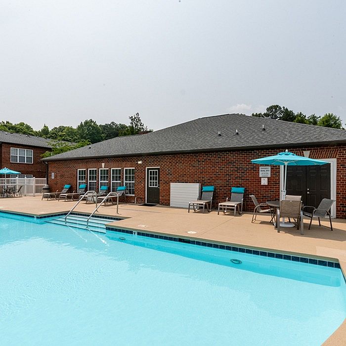 Charming brick apartment complex with an inviting swimming pool surrounded by cozy lounge chairs and umbrellas.