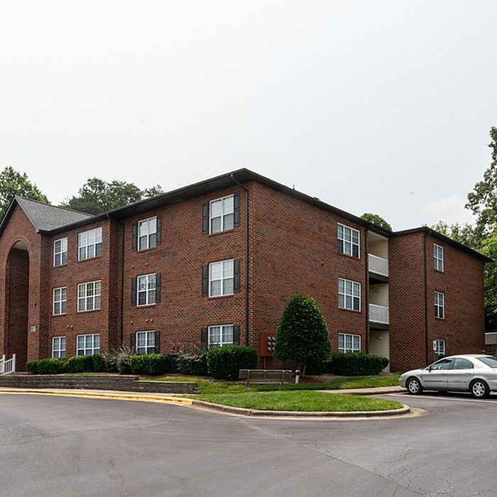 Charming brick apartment building with lush greenery and ample parking, offering a serene residential appeal.