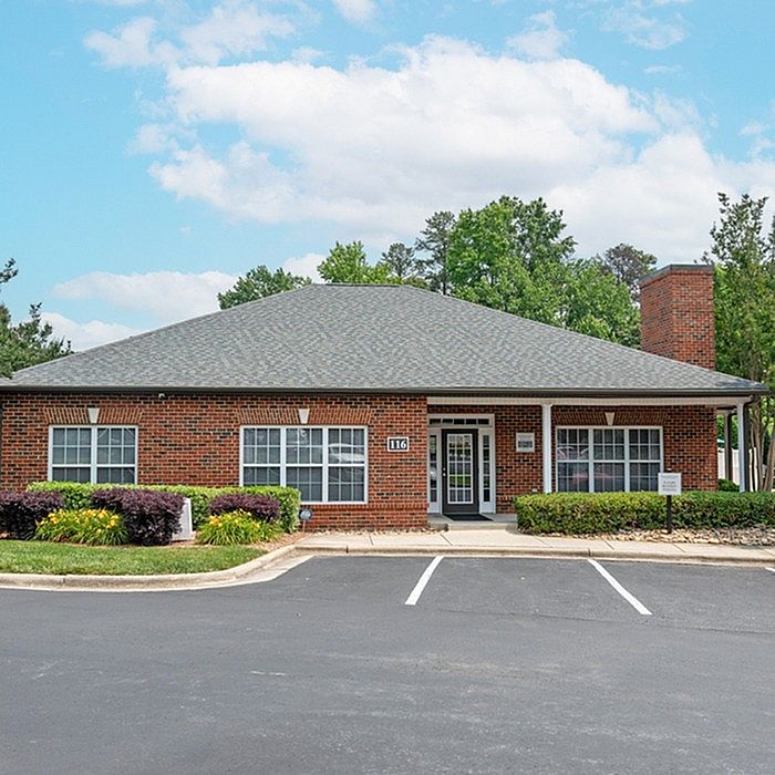 Charming brick apartment building with lush landscaping and ample parking, nestled in a serene suburban setting.