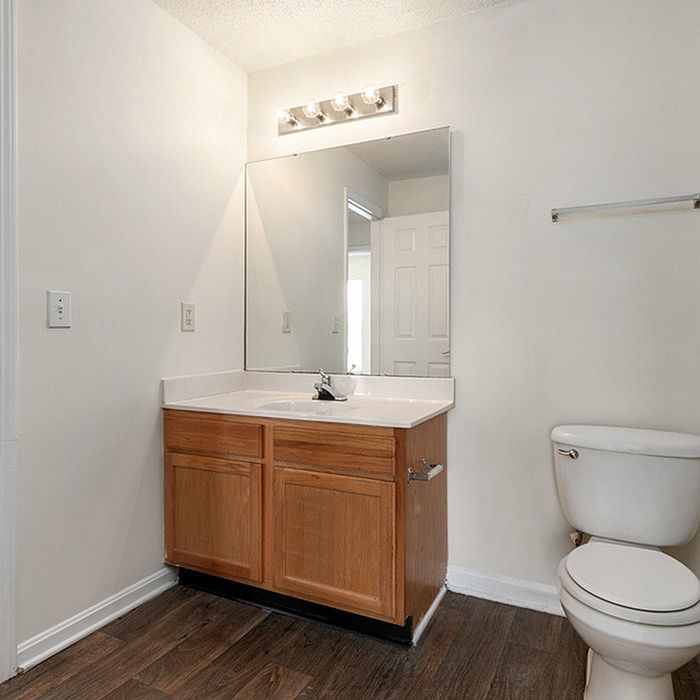 Elegant bathroom with modern lighting, spacious mirror, wooden vanity, and pristine toilet, perfect for contemporary living.