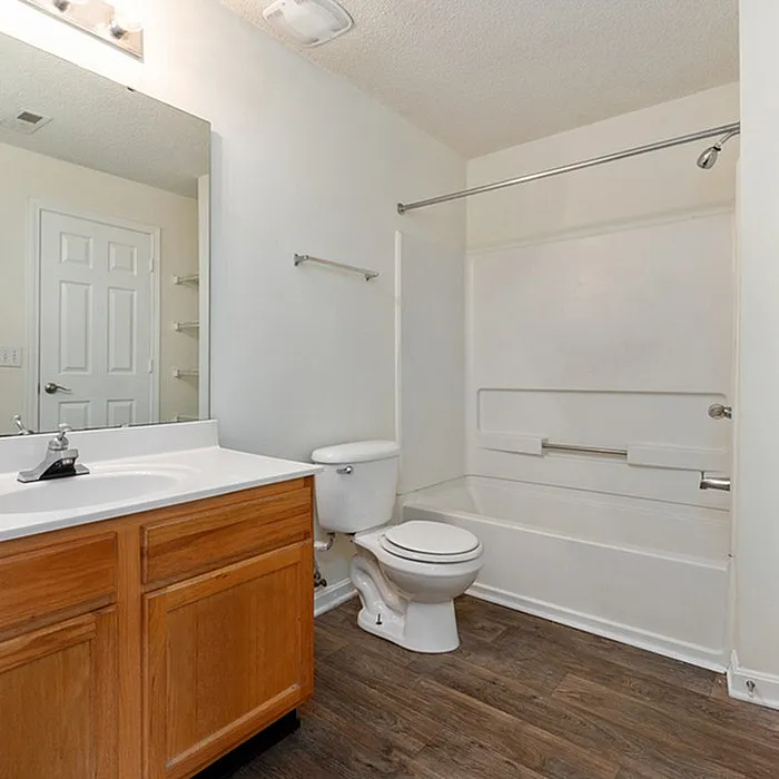Bright and modern bathroom featuring elegant wood cabinetry, sleek white fixtures, and a spacious bathtub on stylish wooden flooring.