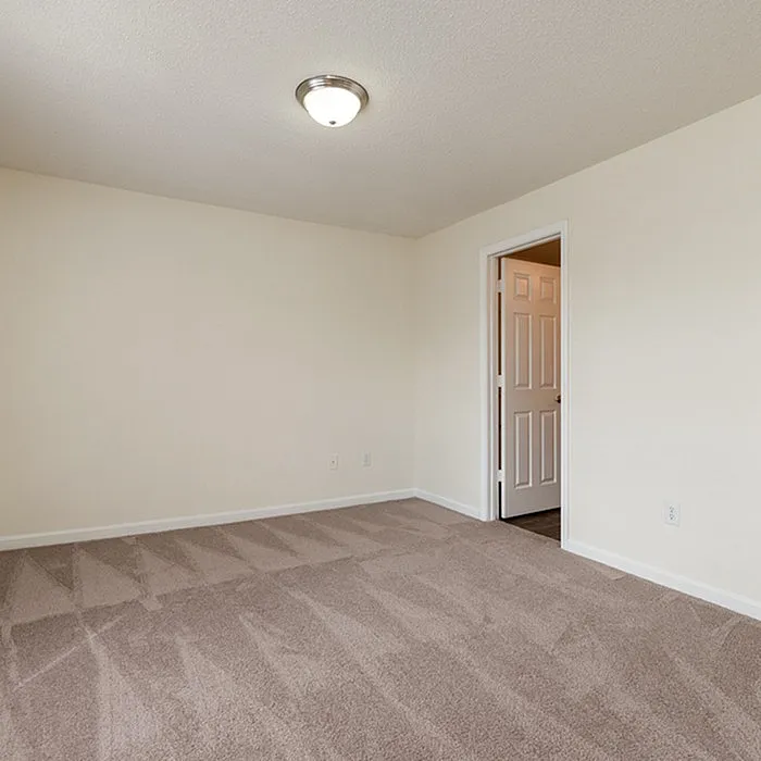Inviting bedroom with plush carpeting, neutral walls, and natural light flooding through an open doorway.