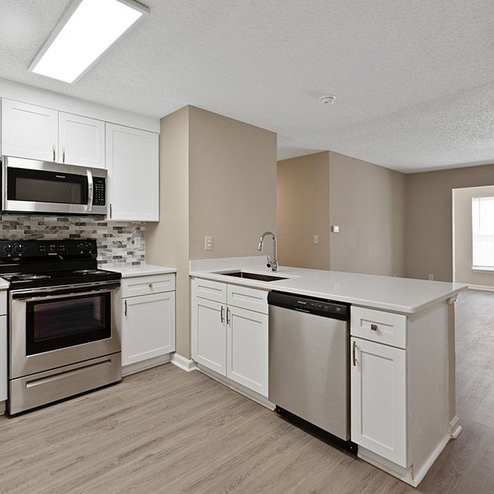 Modern kitchen with sleek stainless steel appliances, elegant white cabinetry, and a stylish backsplash, flowing into a bright open living area.