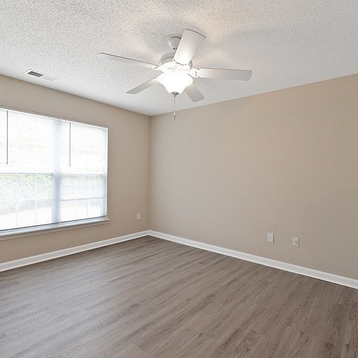 Bright and airy room with elegant gray flooring and large window, enhanced by a ceiling fan for modern comfort.