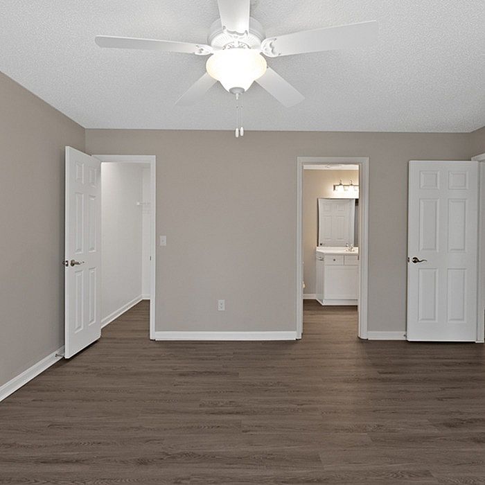 Modern bedroom with sleek wood flooring, elegant ceiling fan, and en-suite bathroom, offering bright and inviting space.