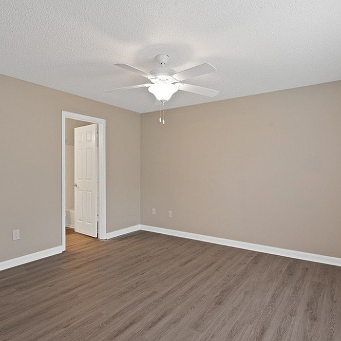 Bright and spacious bedroom with elegant wood flooring, featuring a modern ceiling fan and a doorway leading to an adjacent room.