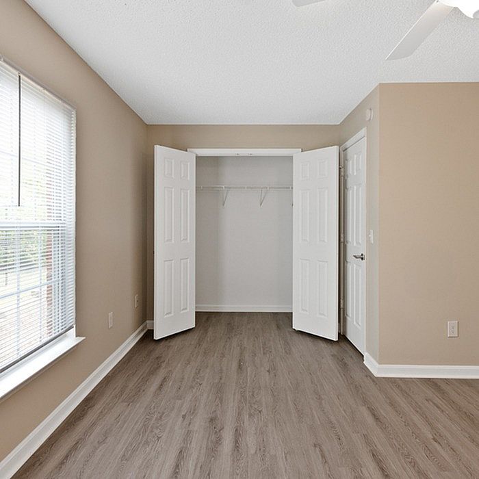 Bright bedroom with elegant wooden floors, large window for natural light, and spacious closet with double doors.