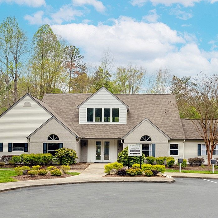 Charming residential building with a classic gable roof and lush landscaping, set against a backdrop of vibrant greenery and blue skies.