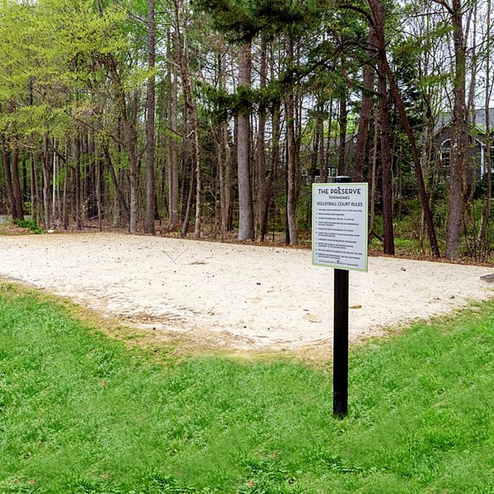 Serene outdoor sand volleyball court surrounded by lush greenery and tall trees, offering a perfect spot for recreation and leisure.
