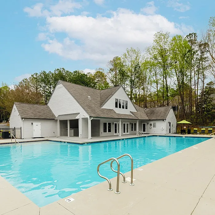 Inviting outdoor swimming pool beside a charming clubhouse surrounded by lush greenery, perfect for relaxation and leisure.