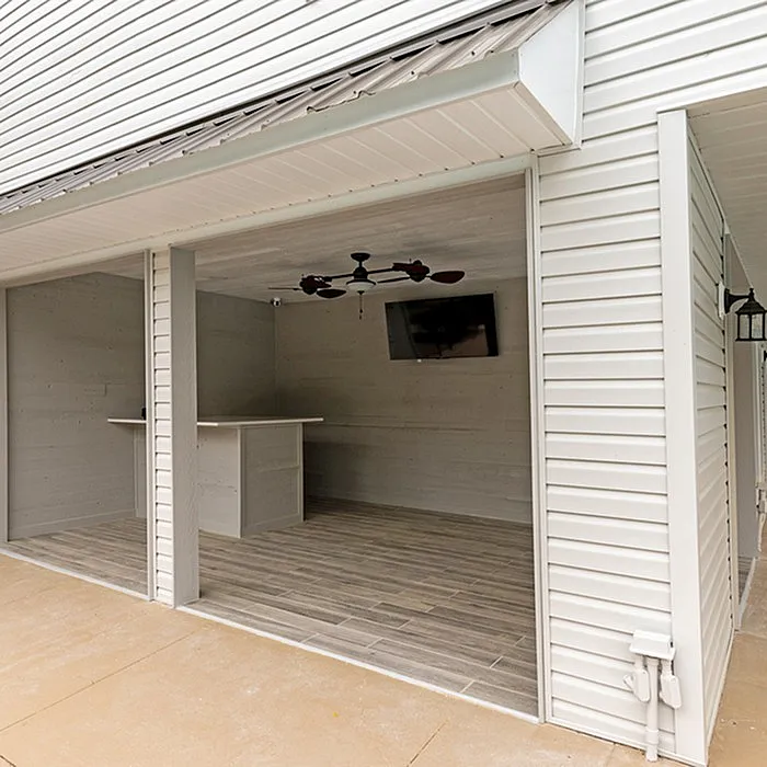 Spacious outdoor covered area featuring elegant wood paneling, ceiling fan, and mounted TV, perfect for entertaining guests.