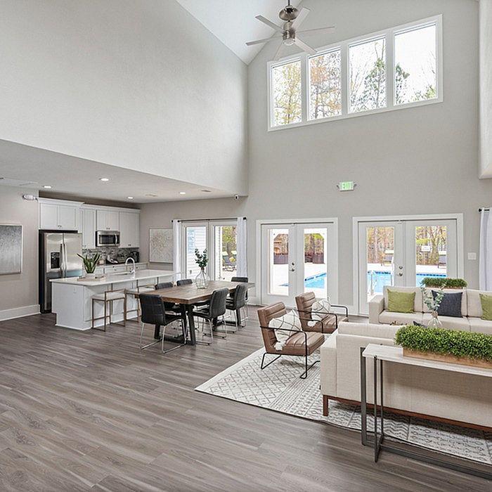 Modern open-plan living area with high ceilings, sleek kitchen, and cozy seating, overlooking a bright poolside view.