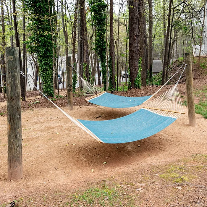Serene outdoor space featuring two blue hammocks nestled among tall trees, offering a perfect relaxation spot.