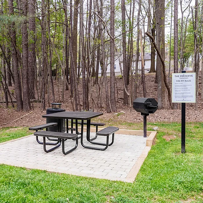 Charming outdoor picnic area with a grill and seating in a serene forest setting, perfect for gatherings and relaxation.
