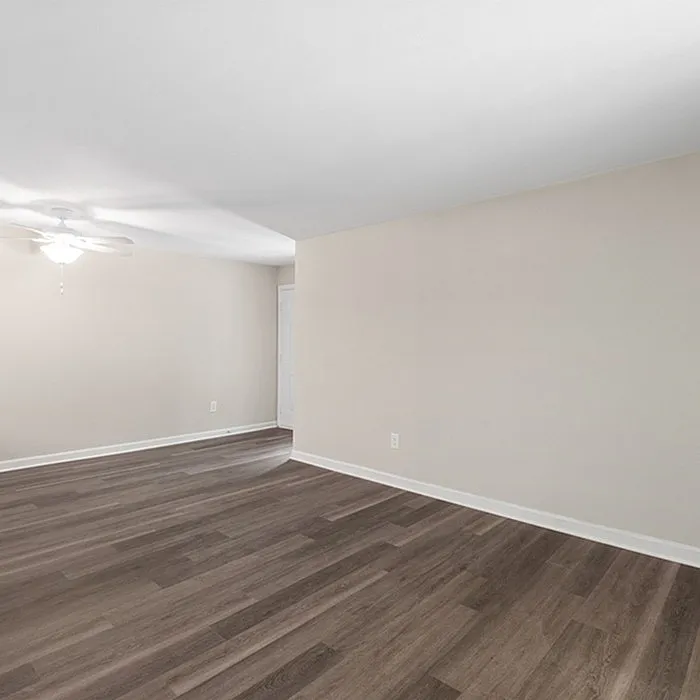 Spacious room with elegant dark wood flooring and soft neutral walls, enhanced by a ceiling fan for comfort.