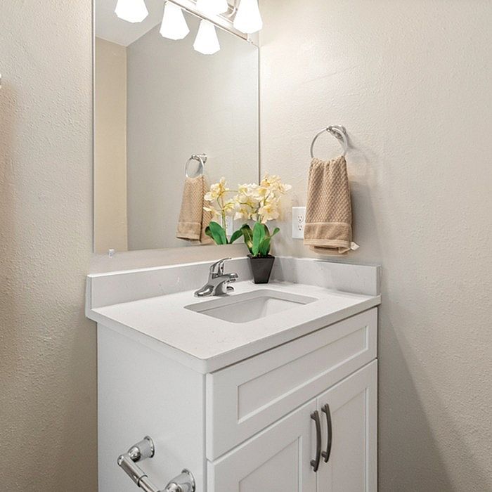 Modern bathroom vanity with a sleek white countertop, elegant mirror, and decorative flowers for a touch of luxury.