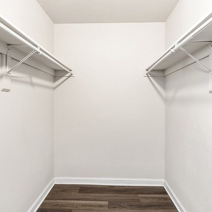 Spacious walk-in closet with white walls and elegant hardwood flooring, perfect for ample storage.